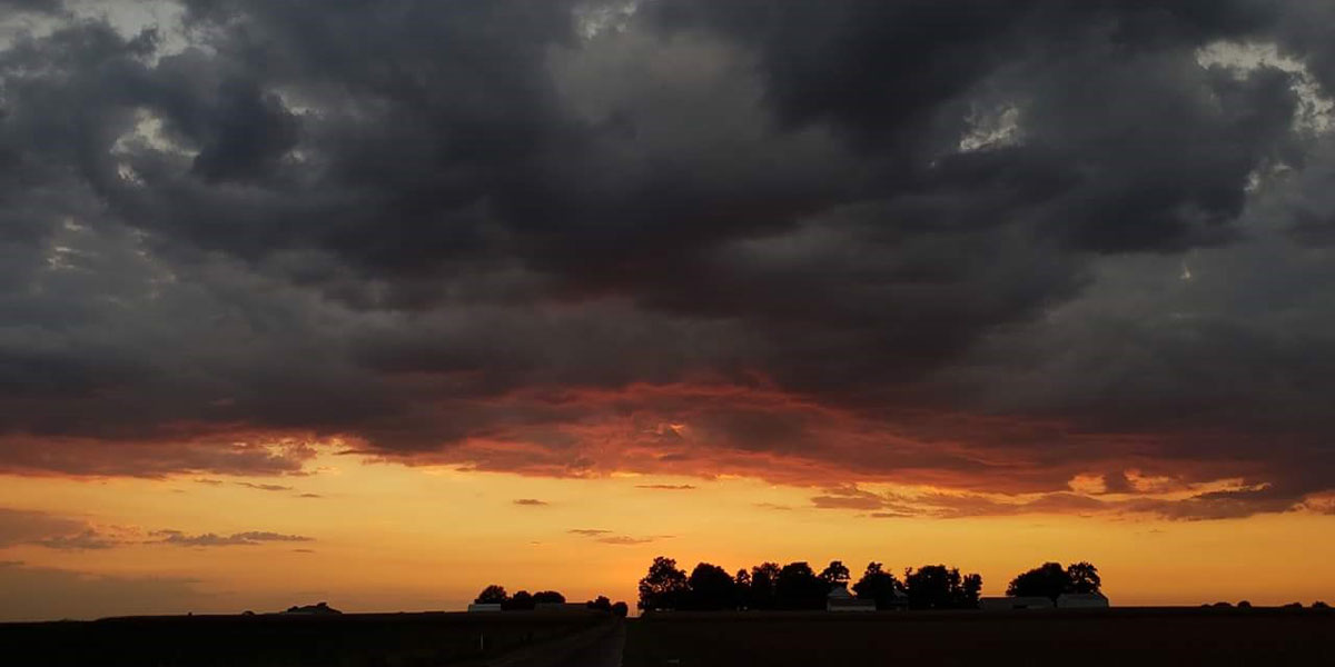 Storm clouds over the silhouette of a farm at sunset